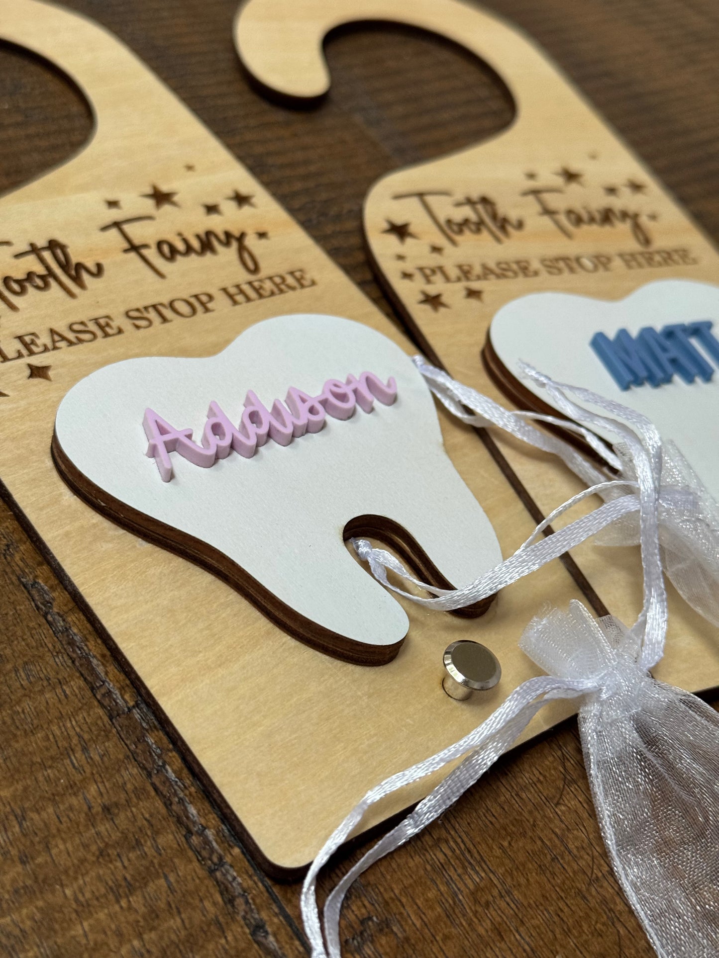 Wooden tooth-shaped door hangers with 'Tooth Fairy' text and personalized names on a wooden surface.