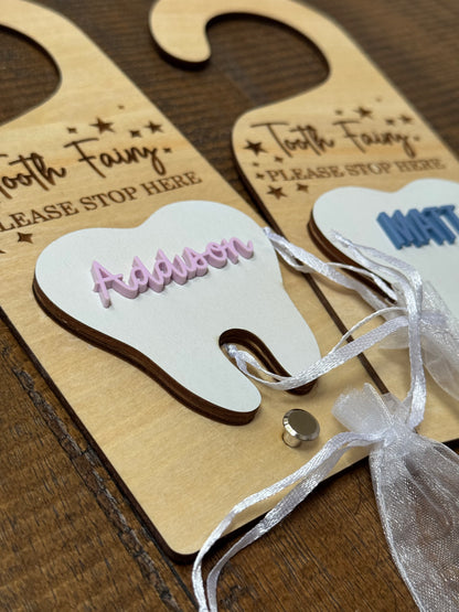 Wooden tooth-shaped door hangers with 'Tooth Fairy' text and personalized names on a wooden surface.
